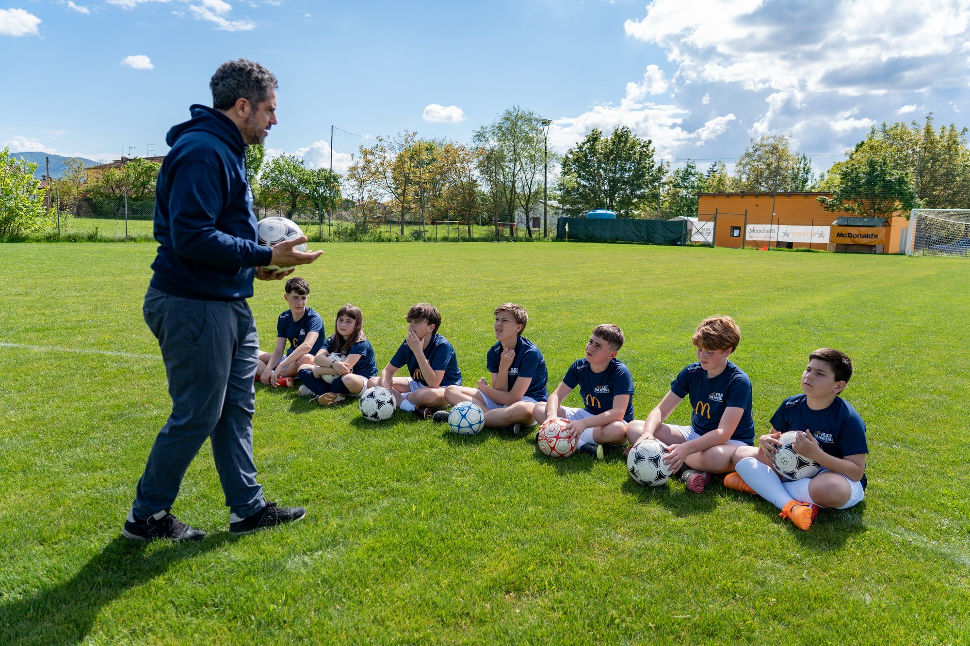 Gruppo di ragazzi seduti sul campo che ascoltano lo staff prima dell'allenamento